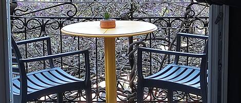 Un balcón con una mesa redonda y dos sillas, una pequeña planta en maceta y una toalla doblada sobre un tapete azul.