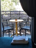 Un balcon avec une table ronde et deux chaises, une petite plante en pot et une serviette pliée posée sur un tapis bleu.