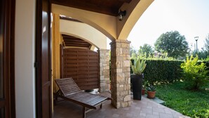 Ein überdachter Patio-Bereich mit einer Holzbank, Steinpfeilern und Topfpflanzen.