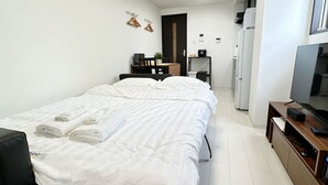 Et moderne hotelværelse med en stor seng, et skrivebord med stol, et fjernsyn og et lille tekøkken.