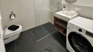 A modern bathroom with a toilet, sink, shower, and a washing machine.