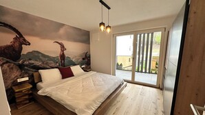 A modern bedroom with a large bed, wooden flooring, a mural of animals, and a sliding glass door to the outside.