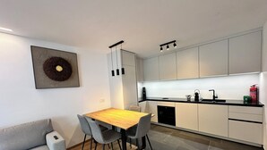 A modern kitchen with white cabinets, a wooden dining table, and a gray sofa.