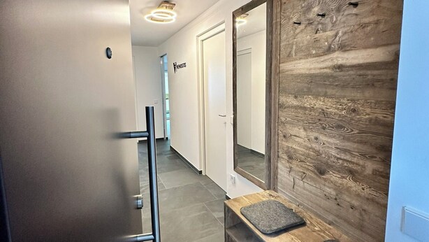 A modern hallway with a bench, a wooden accent wall, and a door labeled "FENOSTIS."
