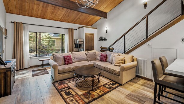 A spacious living room with a wooden ceiling, a large window, a beige sectional sofa, a round coffee table, and a staircase. - 32 Forest Pines | 3BR/2BA Incline Village, Pool (Incline Village)