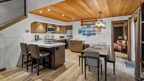 A modern kitchen with a wooden ceiling, a central island with bar stools, and a dining area with a table and chairs. - 32 Forest Pines | 3BR/2BA Incline Village, Pool (Incline Village)