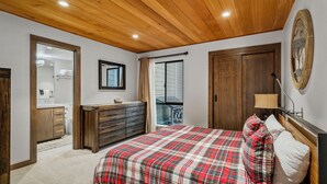 A bedroom with a wooden ceiling, a bed with a plaid bedspread, a dresser, a mirror, and a window with curtains. - 32 Forest Pines | 3BR/2BA Incline Village, Pool (Incline Village)