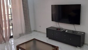 Ett modernt vardagsrum med en platt-TV som är monterad på väggen, ett mörkt träskåp och ett soffbord i glas.