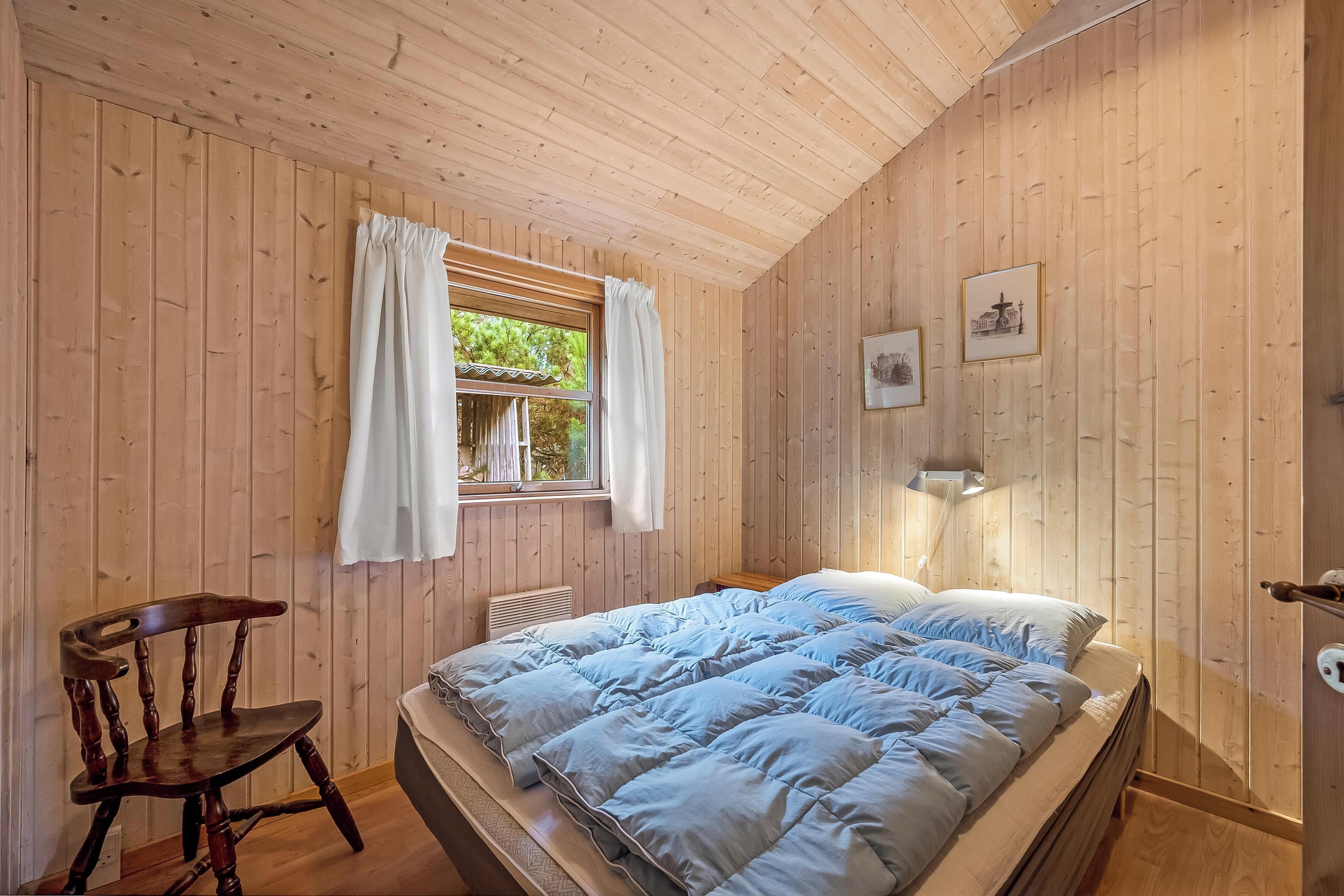 Une pièce aux murs lambrissés, comprenant un lit, une chaise et une fenêtre avec des rideaux.