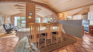 Un comedor amplio con una mesa larga y sillas, una cocina con armarios y electrodomésticos, y una pared de ladrillo con una ventana.