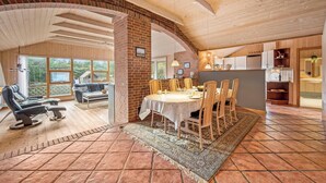 Amplia sala de estar con mesa de comedor, sillas y sofá. Se observa una pared de ladrillo y techo de madera.