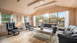 Amplia sala de estar con pisos y paredes de madera, ventanas grandes, un sofá de cuero negro, un sillón de cuero negro y una mesa de centro.