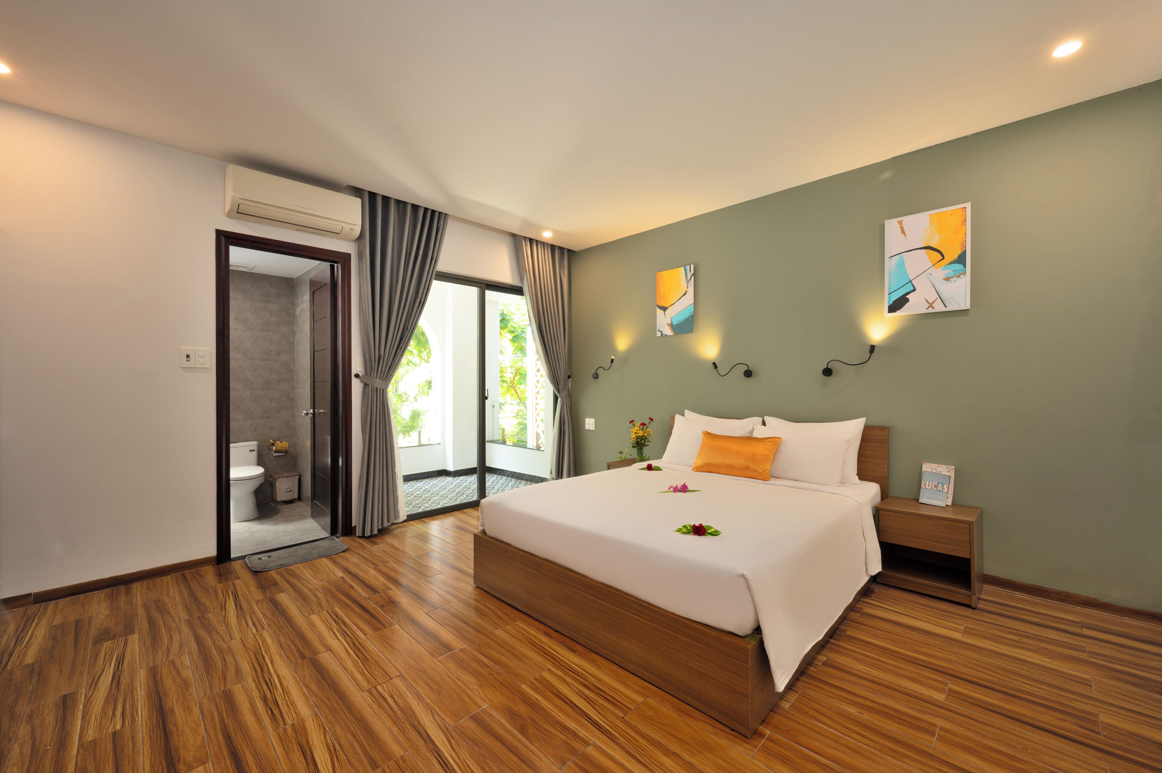 A modern hotel room with a wooden floor, a large bed with white linens, a nightstand, and a painting on the wall.