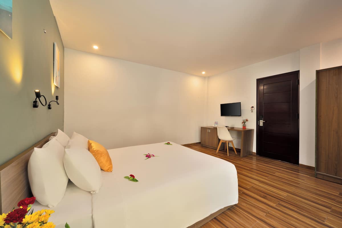 A hotel room with a bed, a desk, a chair, a TV, and a wooden floor.