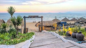 Un sendero de madera que conduce a una playa con sombrillas de paja y sillas de descanso.