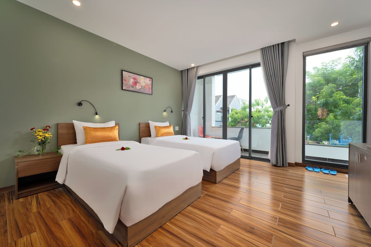 A hotel room with two beds, a large window, and a view of greenery outside.