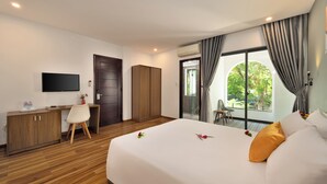 Habitación de hotel con cama, escritorio, silla, televisor y vistas al verde exterior.