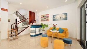 Un moderno vestíbulo de hotel con una escalera, mostrador de recepción, sofá amarillo y un cartel grande en la pared.