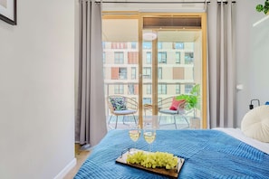 Ein Schlafzimmer mit einem Bett, einer Weintablett mit Trauben, zwei Weingenüssen und einem Balkon mit Stühlen und einer Pflanze.