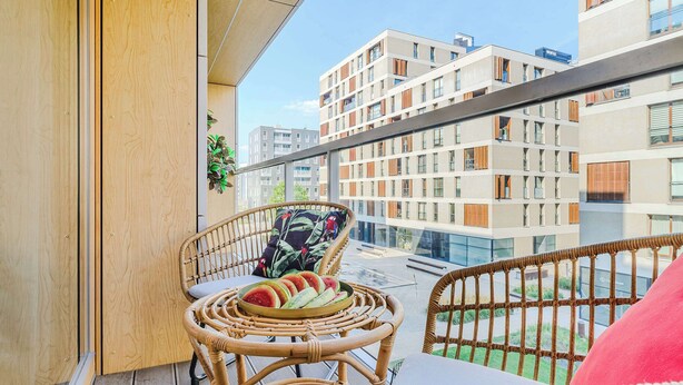 Ein Balkon mit Korbmöbeln, einer Fruchtplatte und Blick auf moderne Gebäude.