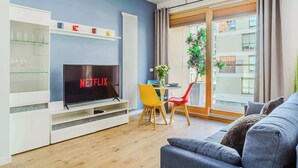 Ein Wohnzimmer mit Fernseher, einer Couch, einem Esstisch mit Stühlen und Blick ins Freie.