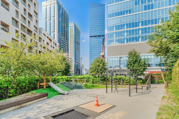A modern urban park with playground equipment, a small slide, and a well-maintained green space.