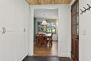 A hallway leading to a dining area with a wooden table and chairs, a window with a view of the outside, and a door with a coat hook.