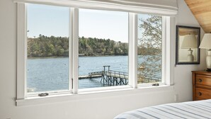 A bedroom with a large window overlooking a lake and dock. - Moon Tide Cottage | Oceanfront on Linekin Bay | Stunning Views (Boothbay Harbor)