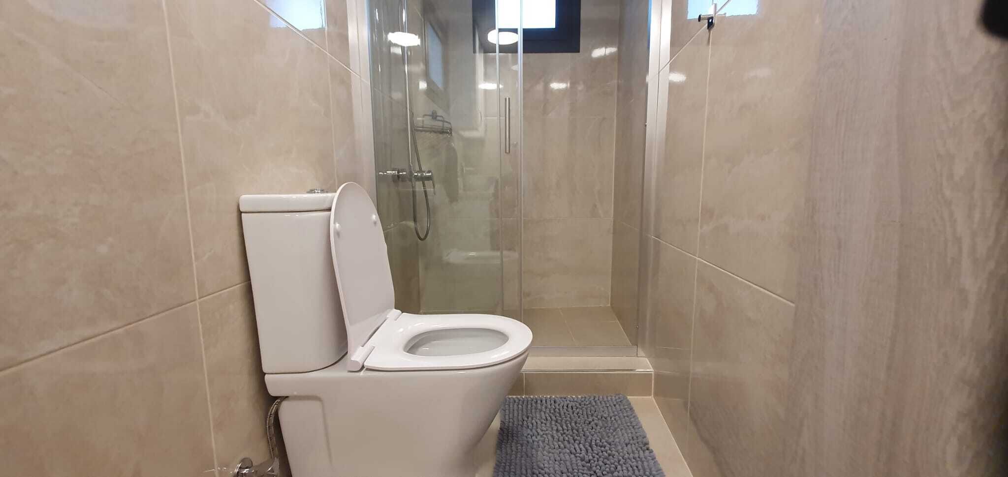 Un baño con inodoro, cabina de ducha de vidrio y paredes de azulejos.