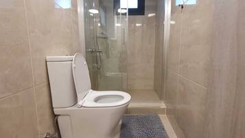 Un baño con inodoro, cabina de ducha de vidrio y paredes de azulejos.