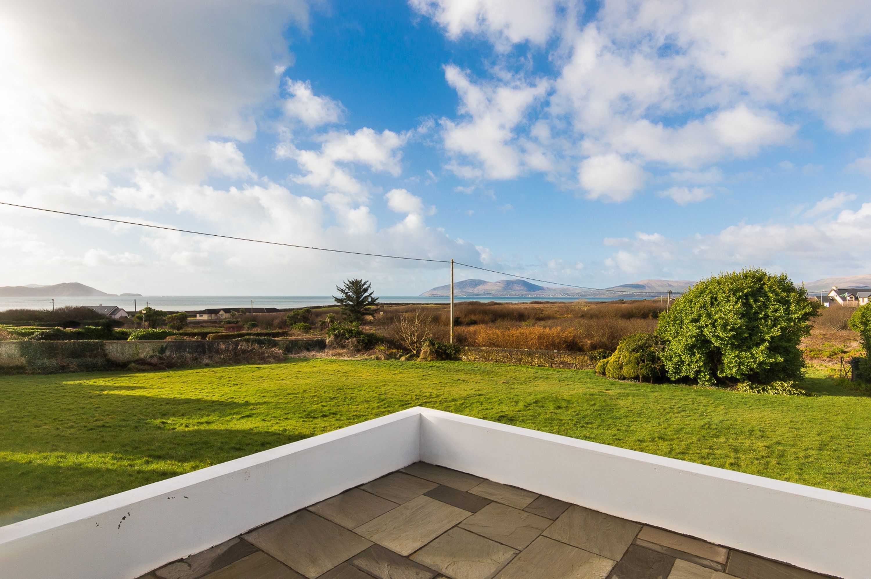 A terrace with a view of a grassy field, a tree, and distant mountains.