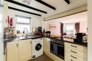 A compact kitchen with a washing machine, a coffee maker, and a toaster. - Cosy two Bedroom Cottage in Waterville With sea Views (Waterville)