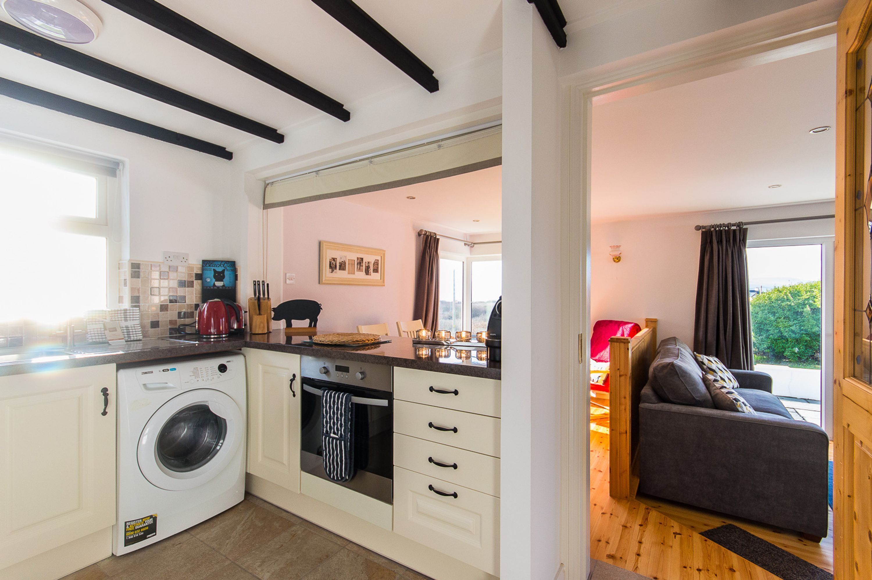 A compact kitchen with a washing machine, oven, and a dining area with a sofa and table.