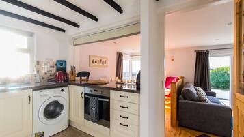 A compact kitchen with a washing machine, oven, and a dining area with a sofa and table.