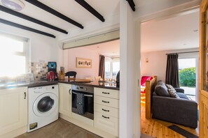 A compact kitchen with a washing machine, oven, and a dining area with a sofa and table. - Cosy two Bedroom Cottage in Waterville With sea Views (Waterville)