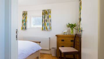 A bedroom with a bed, wooden dresser, chair, radiator, window, and curtains.