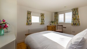 Quarto com cama, penteadeira, cadeira e janela com cortinas.