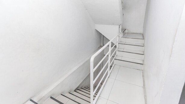 A narrow, white stairwell with metal railings and a tiled floor. - OYO 94348 Bro & Sis (Bekasi)