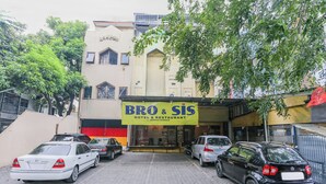 A hotel named "BRO & SIS" with a signboard, parked cars, and a building with a red and yellow facade. - OYO 94348 Bro & Sis (Bekasi)