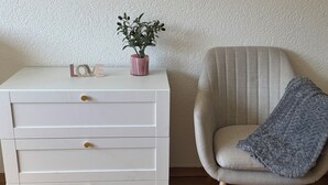 A white dresser with drawers, a pink plant, and the word "LOVE" on top. A grey armchair with a blue throw blanket is next to it. - FriHome Centre Ville (Fribourg)