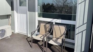 A balcony with two chairs, a white door, and a window overlooking a tree-lined street. - Studio  apartment w/balcony-Nob Hill, UNMH, Pres Hosp. (Albuquerque)
