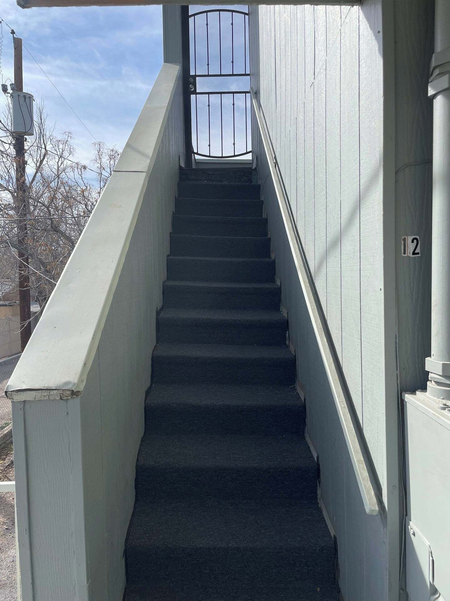 Una escalera metálica que conduce a un edificio, con una puerta al final y un cartel con el número 12.