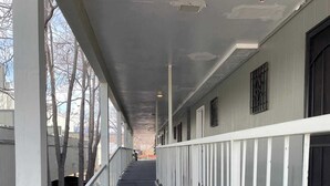 A corridor with white railings, a grey floor, and a grey ceiling with visible wear. - Studio  apartment w/balcony-Nob Hill, UNMH, Pres Hosp. (Albuquerque)