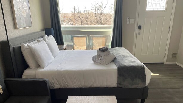 A modern bedroom with a large bed, a dark sofa, and a wooden coffee table. - Studio  apartment w/balcony-Nob Hill, UNMH, Pres Hosp. (Albuquerque)
