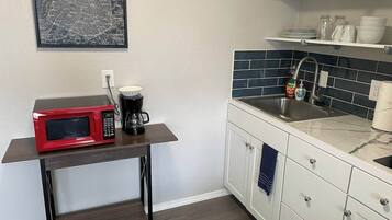 Cocina compacta con microondas, cafetera y pileta con un protector de salpicaduras azul.