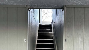 A narrow stairway with a dark carpet, flanked by light-colored walls, leading to a door at the top. - Studio Apartment w/balcony near Nob Hill, UMM and downown. (Albuquerque)
