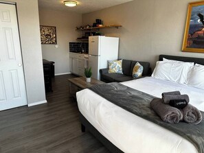 Una habitación de hotel compacta con cama, un escritorio pequeño y una kitchenette.