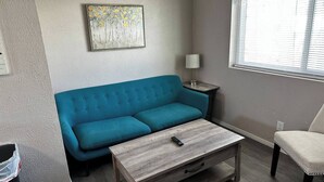 Un salon avec un canapé de couleur turquoise, une table basse en bois, une lampe et un tableau accroché au mur.