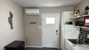 Une cuisine compacte avec un réfrigérateur, une cuisinière et un four à micro-ondes, tous de couleur blanche. On y trouve également un meuble noir et une porte blanche dotée d’une fenêtre.