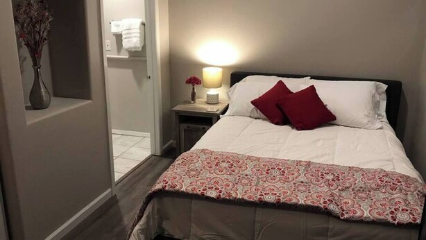 Hotellihuone, jossa on sänky, yöpöytä lampun kanssa, maljakko kuivakukilla ja ovi, joka johtaa kylpyhuoneeseen.
